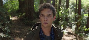 Movie still from “13 Reasons Why” (2017), created by Brian Yorkey – A young man in a jacket is standing in the woods; Close Up shot, Over the shoulder angle
