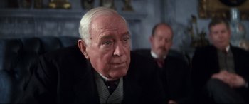 Movie still from “Ragtime” (1981), directed by Milos Forman – An older man in a suit and tie looking at the camera; Close Up shot, Over the shoulder angle