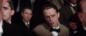 Movie still from “Ragtime” (1981), directed by Milos Forman – A man in a suit and bow tie looking at the camera; Close Up shot, Over the shoulder angle
