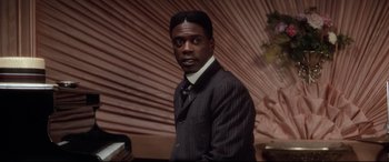 Movie still from “Ragtime” (1981), directed by Milos Forman – A man wearing a suit and tie standing in front of a wall; Close Up shot, High angle