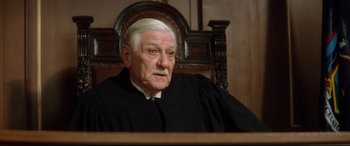 Movie still from “Ragtime” (1981), directed by Milos Forman – An older man in a black robe sitting in a courtroom; Close Up shot, High angle