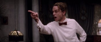 Movie still from “Ragtime” (1981), directed by Milos Forman – A man in a white shirt and a bow tie points to the side; Close Up shot, Low angle