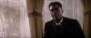 Movie still from “Ragtime” (1981), directed by Milos Forman – A man wearing a suit and tie in front of a window; Close Up shot, Low angle