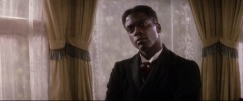 Movie still from “Ragtime” (1981), directed by Milos Forman – A man wearing a suit and tie standing in front of a window; Close Up shot, Low angle