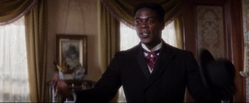 Movie still from “Ragtime” (1981), directed by Milos Forman – A man wearing a suit and tie in a room; Medium shot, Low angle