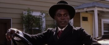 Movie still from “Ragtime” (1981), directed by Milos Forman – A man in a suit and hat standing in front of a building; Close Up shot, Low angle
