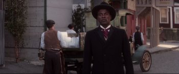 Movie still from “Ragtime” (1981), directed by Milos Forman – A man in a suit and hat standing in front of other men; Medium shot, Low angle