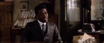 Movie still from “Ragtime” (1981), directed by Milos Forman – A man wearing a suit and tie sitting in a room; Close Up shot, Over the shoulder angle