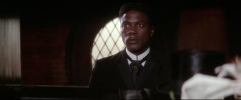 Movie still from “Ragtime” (1981), directed by Milos Forman – A man wearing a suit and tie in front of a stained glass window; Close Up shot, High angle