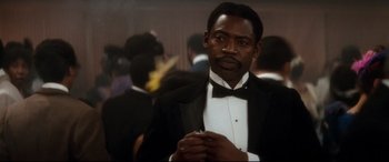 Movie still from “Ragtime” (1981), directed by Milos Forman – A man in a tuxedo is standing in front of a group of people; Close Up shot, Over the shoulder angle