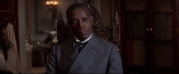 Movie still from “Ragtime” (1981), directed by Milos Forman – An older man wearing a suit and tie sitting in a chair; Close Up shot, Over the shoulder angle