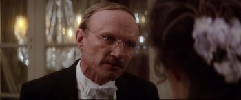 Movie still from “Ragtime” (1981), directed by Milos Forman – An older man wearing a suit and bow tie; Close Up shot, Over the shoulder angle