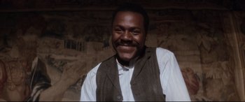 Movie still from “Ragtime” (1981), directed by Milos Forman – A man smiling for the camera in front of a mural; Close Up shot, Low angle