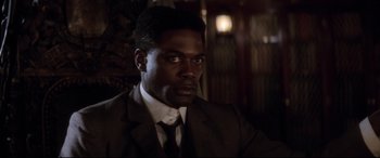 Movie still from “Ragtime” (1981), directed by Milos Forman – A man wearing a suit and tie in a dark room; Close Up shot, High angle