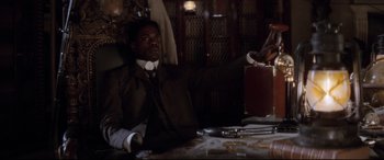 Movie still from “Ragtime” (1981), directed by Milos Forman – A man sitting at a table in a suit and tie; Medium shot, High angle