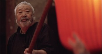 Movie still from “Raise the Red Lantern” (1991), directed by Yimou Zhang – An older man with a beard holding an orange object; Medium shot, Low angle