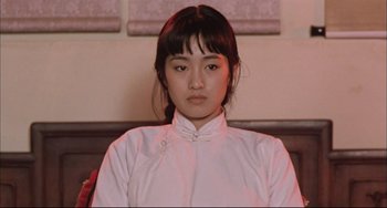 Movie still from “Raise the Red Lantern” (1991), directed by Yimou Zhang – A woman in a white shirt is looking at the camera; Close Up shot, Low angle