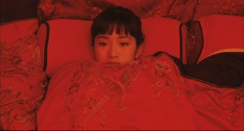 Movie still from “Raise the Red Lantern” (1991), directed by Yimou Zhang – A young woman is laying in a bed with a red blanket; Medium shot, Overhead angle