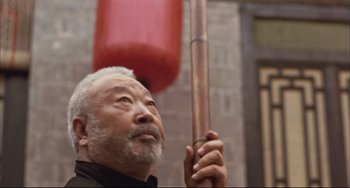 Movie still from “Raise the Red Lantern” (1991), directed by Yimou Zhang – An older man holding a wooden stick in front of a red punching bag; Close Up shot, Low angle