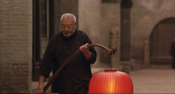 Movie still from “Raise the Red Lantern” (1991), directed by Yimou Zhang – An older man holding an axe near an orange lantern; Medium shot, Low angle