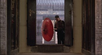 Movie still from “Raise the Red Lantern” (1991), directed by Yimou Zhang – A man holding an open red umbrella in front of a window; Wide shot, Low angle