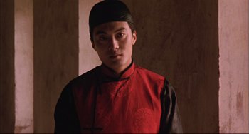 Movie still from “Raise the Red Lantern” (1991), directed by Yimou Zhang – A man in a red and black shirt and a black hat; Medium shot, Low angle