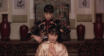 Movie still from “Raise the Red Lantern” (1991), directed by Yimou Zhang – A woman cutting another woman's hair with a hair shears; Medium shot, Over the shoulder angle