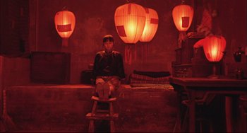 Movie still from “Raise the Red Lantern” (1991), directed by Yimou Zhang – A person sitting on a stool in front of some lights; Wide shot, Overhead angle