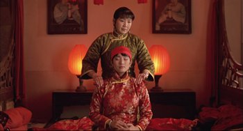 Movie still from “Raise the Red Lantern” (1991), directed by Yimou Zhang – Two women in traditional chinese clothing are sitting on a bed; Medium shot, Low angle