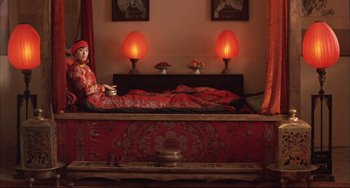 Movie still from “Raise the Red Lantern” (1991), directed by Yimou Zhang – A woman sitting on top of a bed in a room; Wide shot, High angle