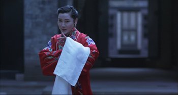 Movie still from “Raise the Red Lantern” (1991), directed by Yimou Zhang – A woman in a red jacket holding a paper towel; Medium shot, Low angle