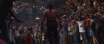 Movie still from “Rambo III” (1988), directed by Peter MacDonald – A man is walking in front of a crowd of people; Wide shot, Low angle