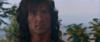 Movie still from “Rambo III” (1988), directed by Peter MacDonald – A person with long curly hair; Close Up shot, Over the shoulder angle