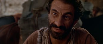 Movie still from “Rambo III” (1988), directed by Peter MacDonald – A person with a beard looking at the camera; Close Up shot, Over the shoulder angle