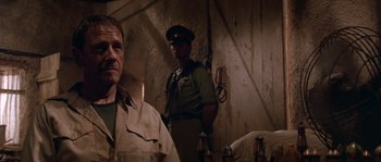 Movie still from “Rambo III” (1988), directed by Peter MacDonald – A man standing next to another man in a room; Close Up shot, Low angle