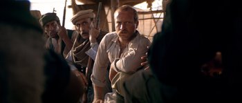 Movie still from “Rambo III” (1988), directed by Peter MacDonald – A man with a gun in his hand and another man with a hat in his hand and another man with a gun in his other hand; Medium shot, Over the shoulder angle