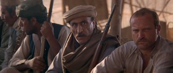 Movie still from “Rambo III” (1988), directed by Peter MacDonald – A man with a hat and a beard holding a rifle; Close Up shot, Low angle