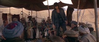 Movie still from “Rambo III” (1988), directed by Peter MacDonald – A group of people sitting under an awning on the ground; Wide shot, Low angle