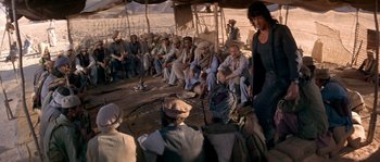 Movie still from “Rambo III” (1988), directed by Peter MacDonald – A group of men sitting around a tent; Wide shot, Over the shoulder angle