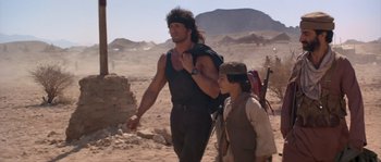 Movie still from “Rambo III” (1988), directed by Peter MacDonald – A man and a woman walking through the desert; Medium shot, Over the shoulder angle