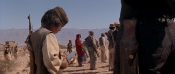 Movie still from “Rambo III” (1988), directed by Peter MacDonald – A group of people standing in the desert; Medium shot, Over the shoulder angle