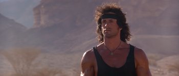 Movie still from “Rambo III” (1988), directed by Peter MacDonald – A man with long hair wearing a black tank top; Close Up shot, Low angle