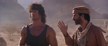 Movie still from “Rambo III” (1988), directed by Peter MacDonald – A man talking to another man on a beach; Medium shot, Over the shoulder angle