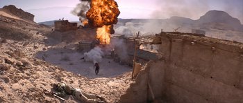 Movie still from “Rambo III” (1988), directed by Peter MacDonald – An explosion is seen in the background of a desert scene; Extreme Wide shot, High angle