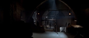 Movie still from “Rambo III” (1988), directed by Peter MacDonald – A person walking in a dark room with lights on; Extreme Wide shot, High angle