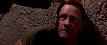 Movie still from “Rambo III” (1988), directed by Peter MacDonald – A person sitting down with his hand on his head; Close Up shot, Over the shoulder angle