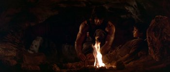 Movie still from “Rambo III” (1988), directed by Peter MacDonald – A man sitting in front of a fire in the dark; Wide shot, Low angle