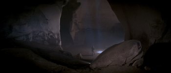 Movie still from “Rambo III” (1988), directed by Peter MacDonald – A man standing in a cave with a light shining on him; Extreme Wide shot, High angle