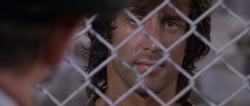 Movie still from “Rambo: First Blood Part II” (1985), directed by George P. Cosmatos – A person behind a chain link fence; Close Up shot, Over the shoulder angle