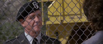Movie still from “Rambo: First Blood Part II” (1985), directed by George P. Cosmatos – An older man in a military uniform behind a chain link fence; Close Up shot, Low angle